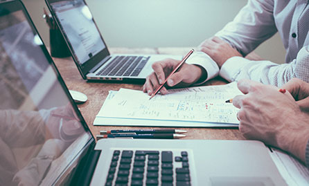 Two men working at a desk with laptops and paperwork